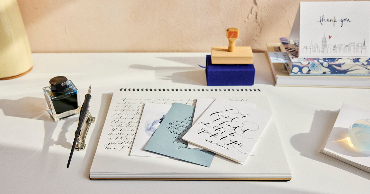 Desk setup with stationery items including a notebook, pen, inkwell, and cards.